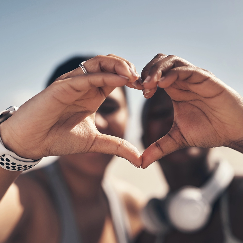 Two people forming a heart shape with their hands while standing close together outdoors.