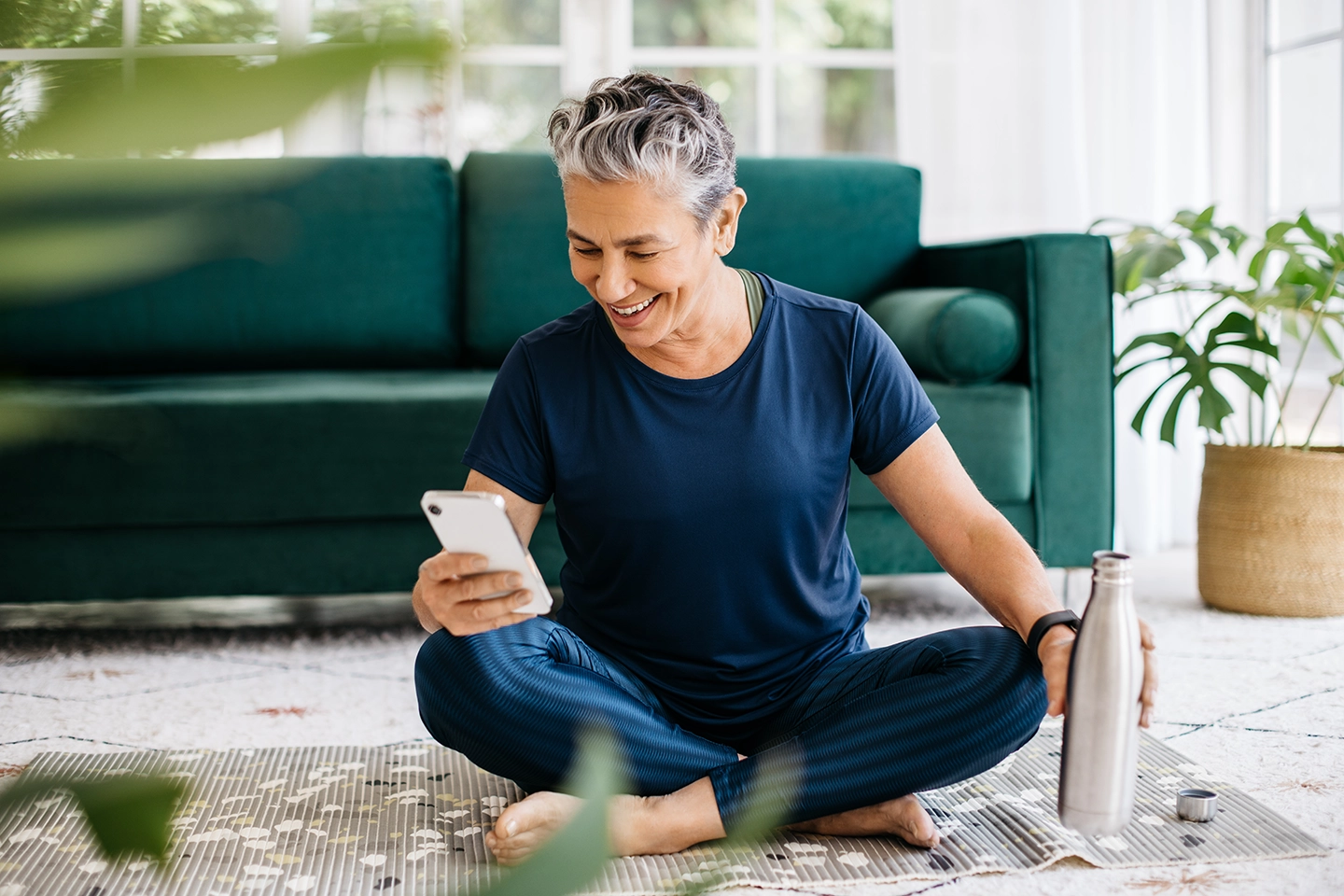 A woman in her 50s sitting on the floor looking at her cell phone smiling.