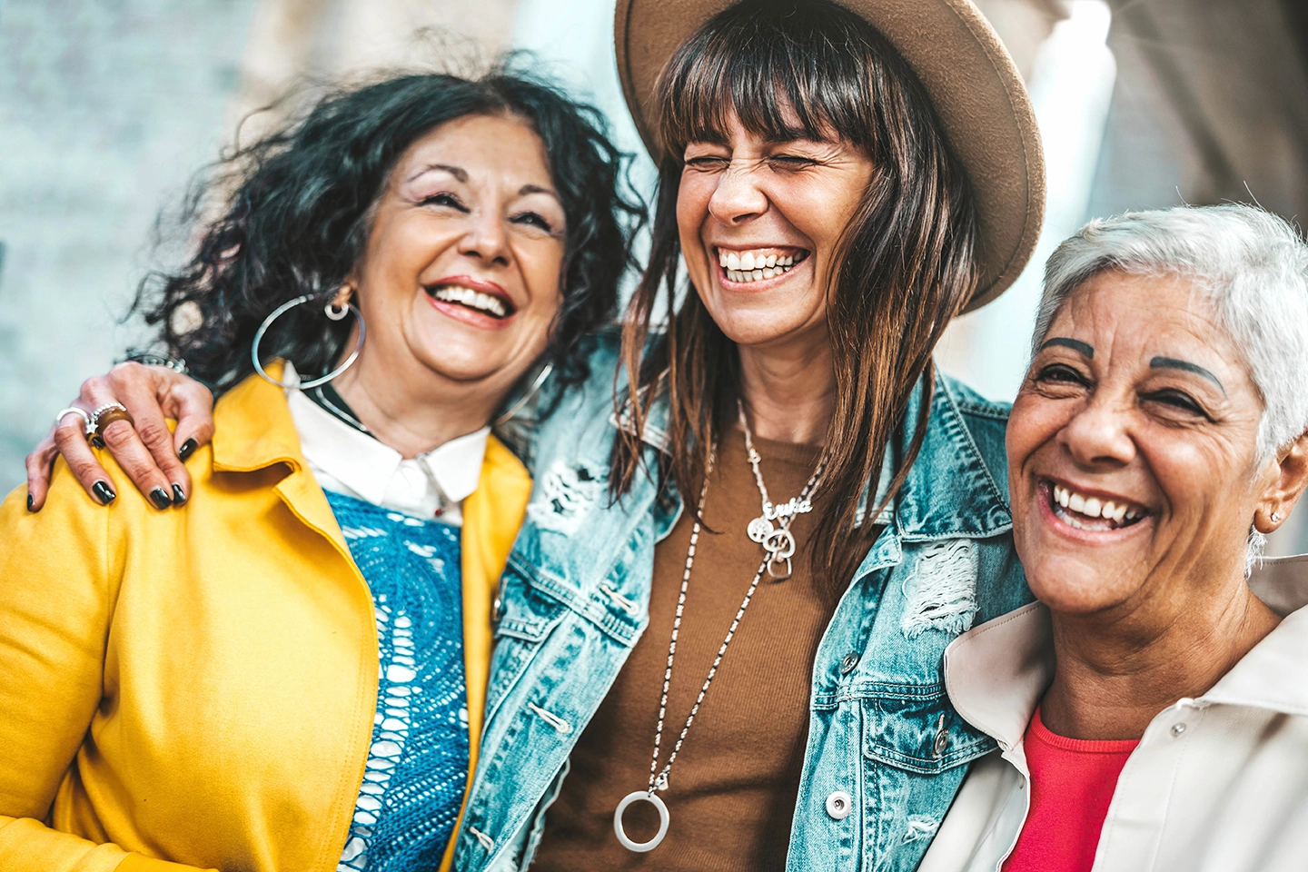 Three women of different ages hanging together outdoors and laughing, representing different life stages