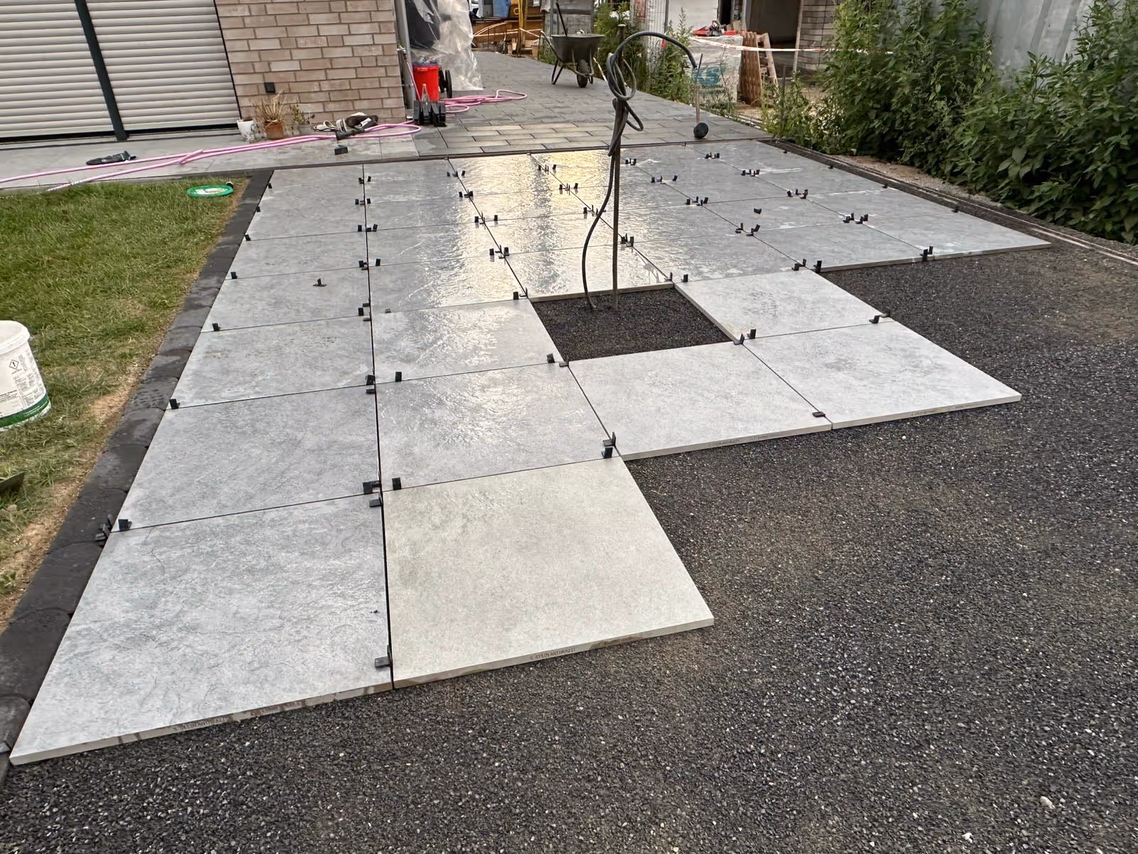 Verlegung von hellen Großformatplatten auf Splittbett mit Fugenkreuzen und dunkler Pflasterung im Hintergrund - Lindemann Bau GmbH