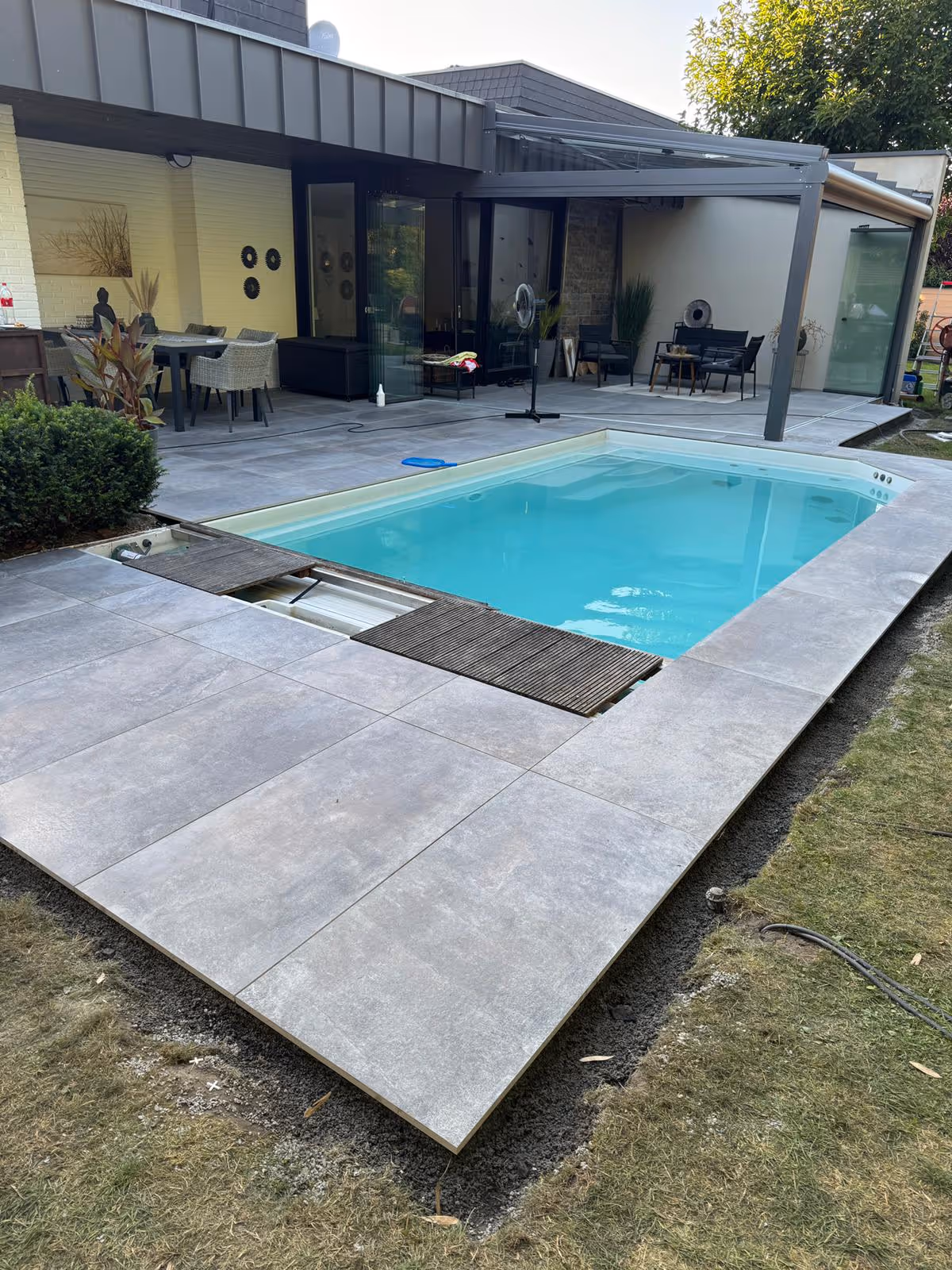 Fertiggestellte Terrasse mit großformatigen Fliesen und in die Fläche integrierter Pool-Abdeckung, geöffnet - Lindemann Bau GmbH