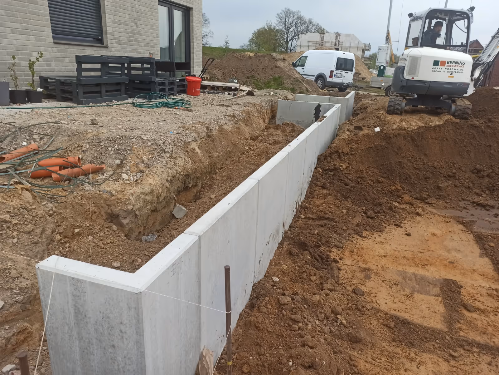 Erstellung einer Stützmauer aus Betonfertigteilen für eine erhöhte Terrasse mit Baugrube im Vordergrund - Lindemann Bau GmbH