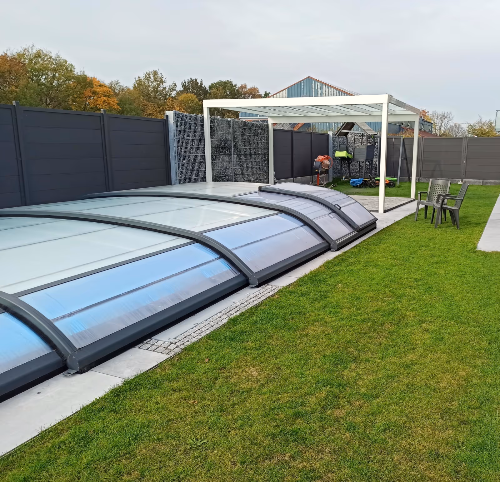 Fertiggestellter Gartenbereich mit verschiebbarer Pool-Überdachung, Gabionenwand und weißer Pergola - Lindemann Bau GmbH