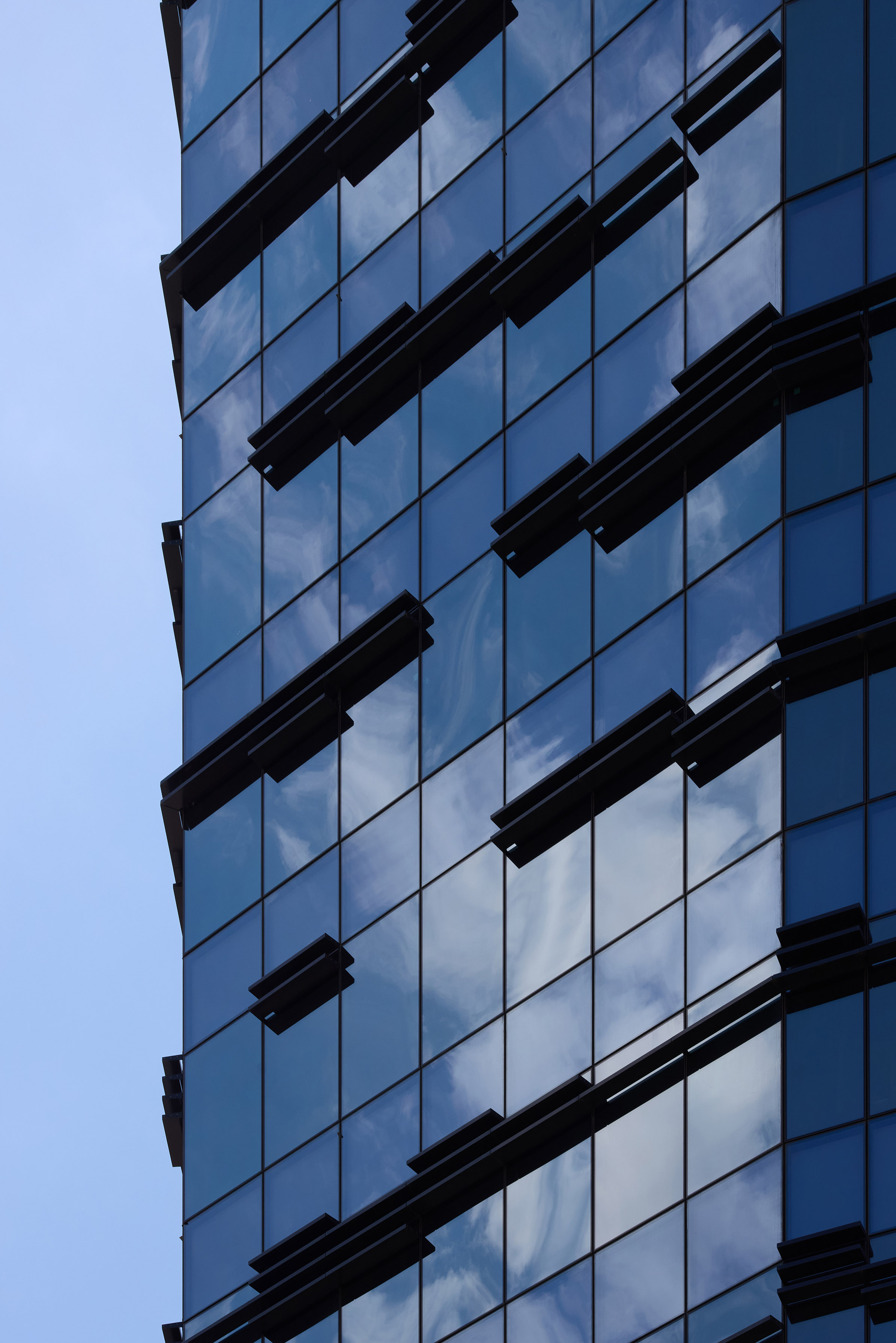 Close-up of a modern glass building facade reflecting the blue sky and white clouds.