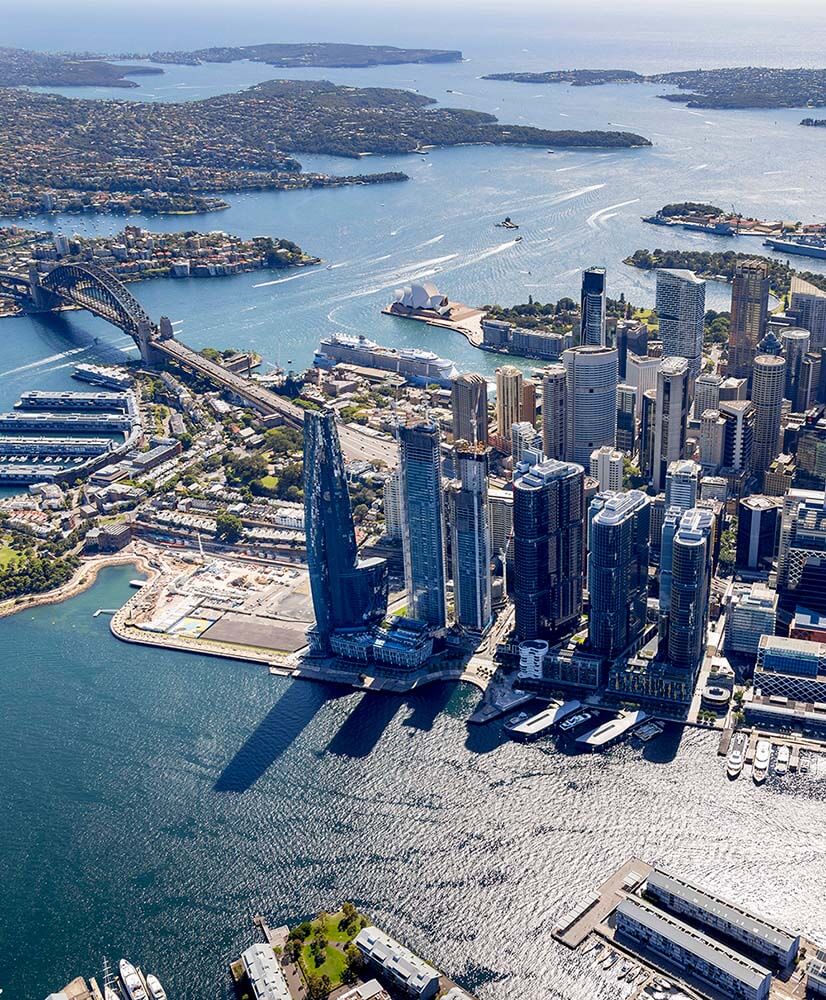 Aerial view of Sydney Harbour featuring Sydney Opera House, Harbour Bridge, and city skyscrapers along the waterfront.