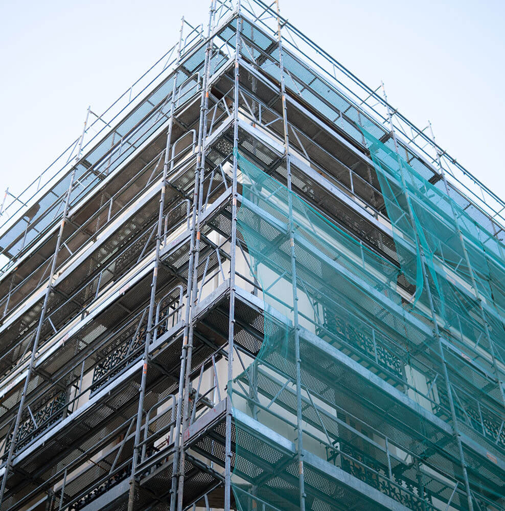 Metal scaffolding with green safety netting covering a building under construction against a clear sky.