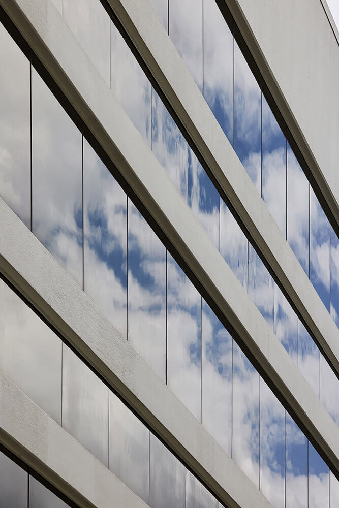 Diagonal view of a modern building facade with reflective glass windows showing a cloudy sky.
