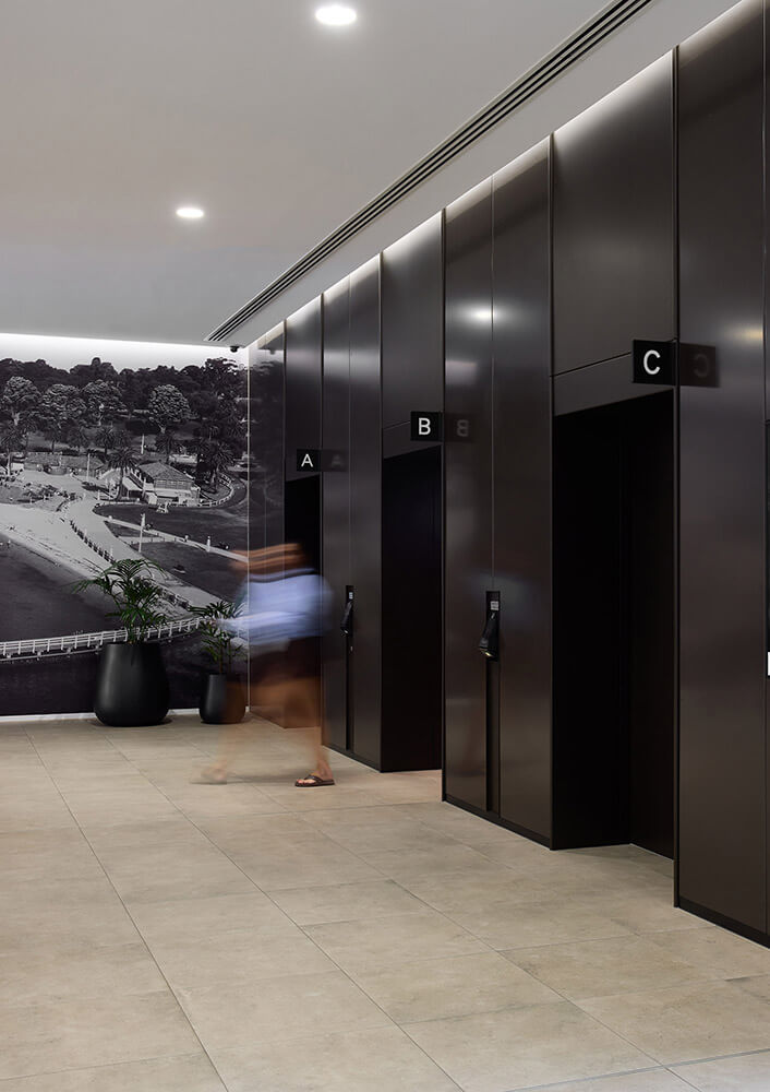 Modern elevator lobby with three black elevators labeled A, B, and C, and a blurred person walking in front.