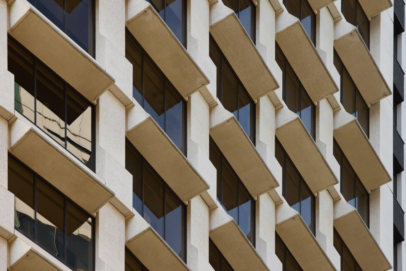 Close-up of a building facade with a repetitive pattern of rectangular windows and angled concrete sunshades.