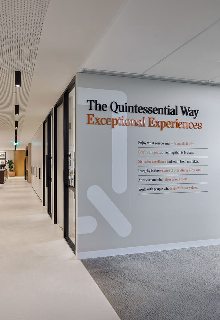 Office hallway with a wall displaying 'The Quintessential Way Exceptional Experiences' and guiding principles.