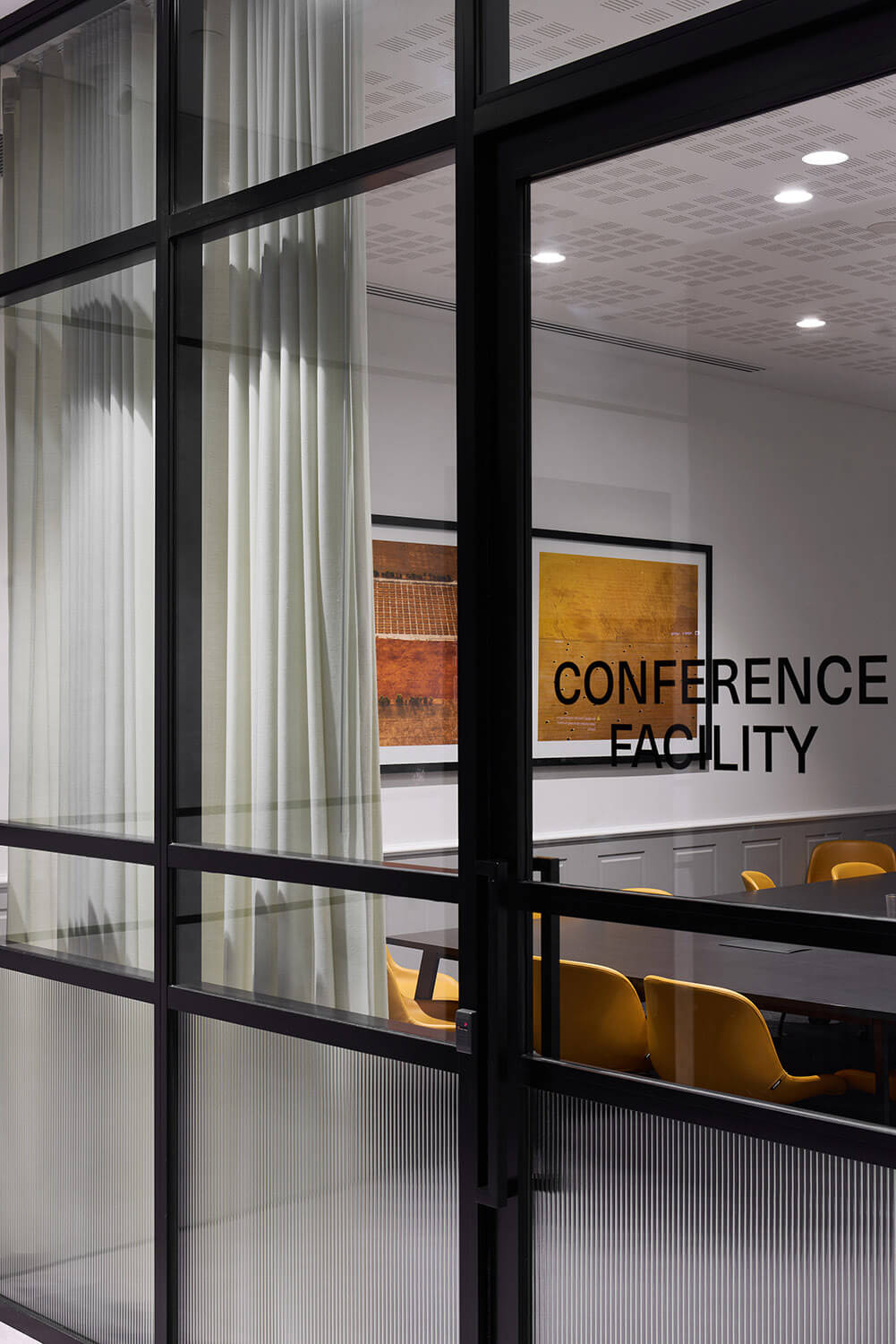 Modern conference room with glass walls, yellow chairs, a long black table, and framed abstract art on the wall.