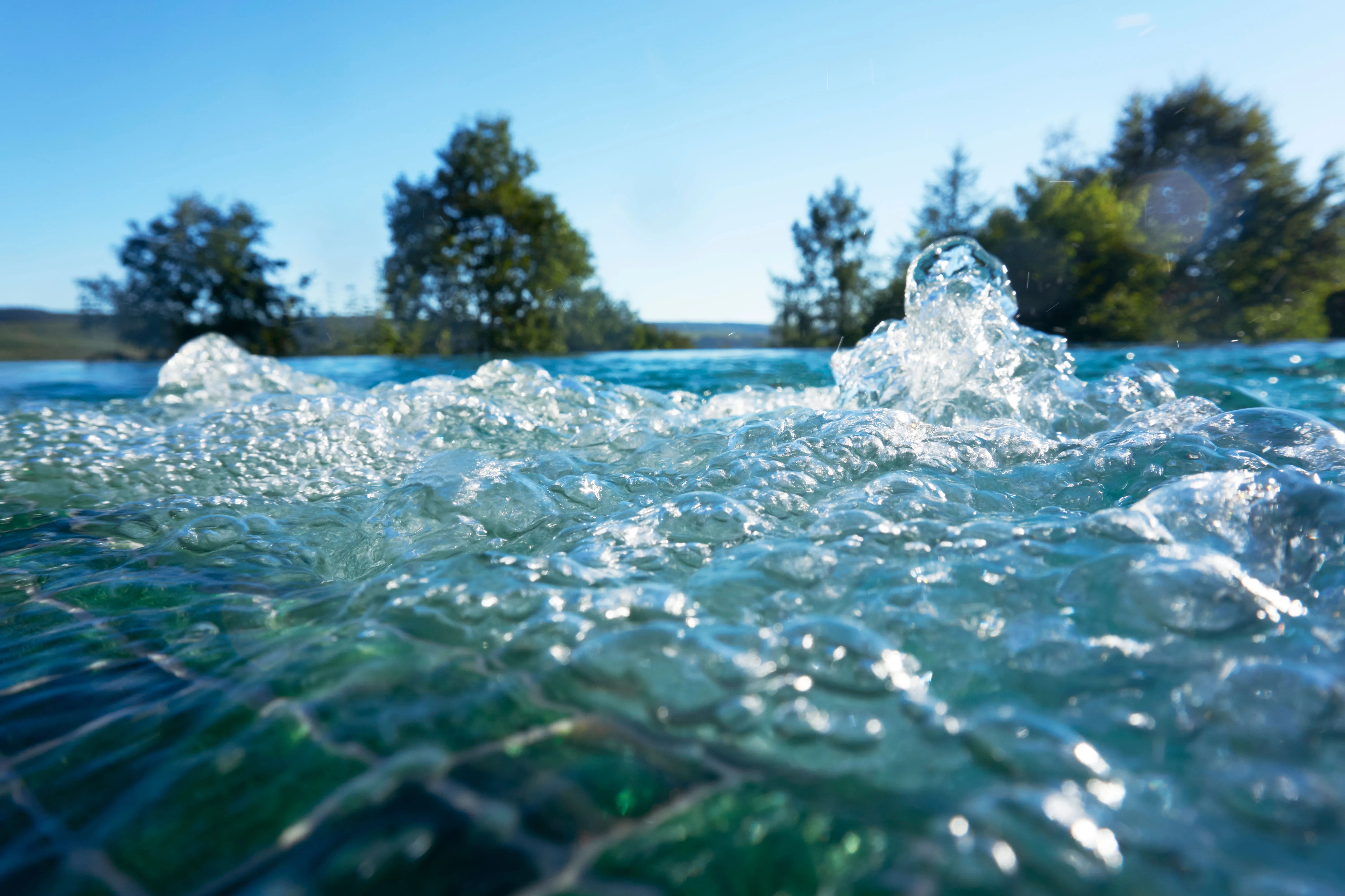 Sprudelndes Wasser in einem Außenpool vor klarem Himmel und Bäumen im Hintergrund.