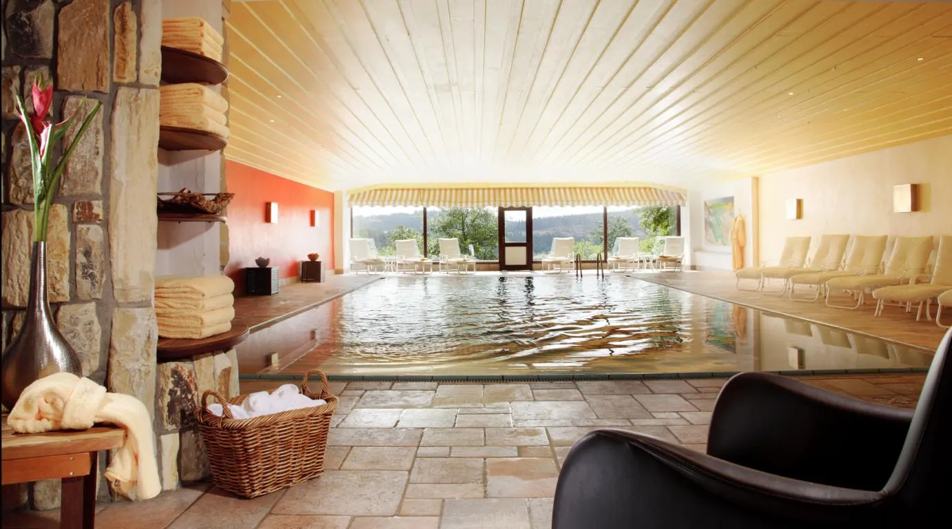 Beheiztes Hallenbad mit Liegestühlen am Fenster, Regalen mit Handtüchern und Korb mit weißen Handtüchern neben Steinsäule.