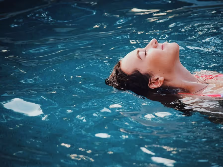 Frau mit geschlossenen Augen, die entspannt auf dem Rücken in einem Becken schwimmt.