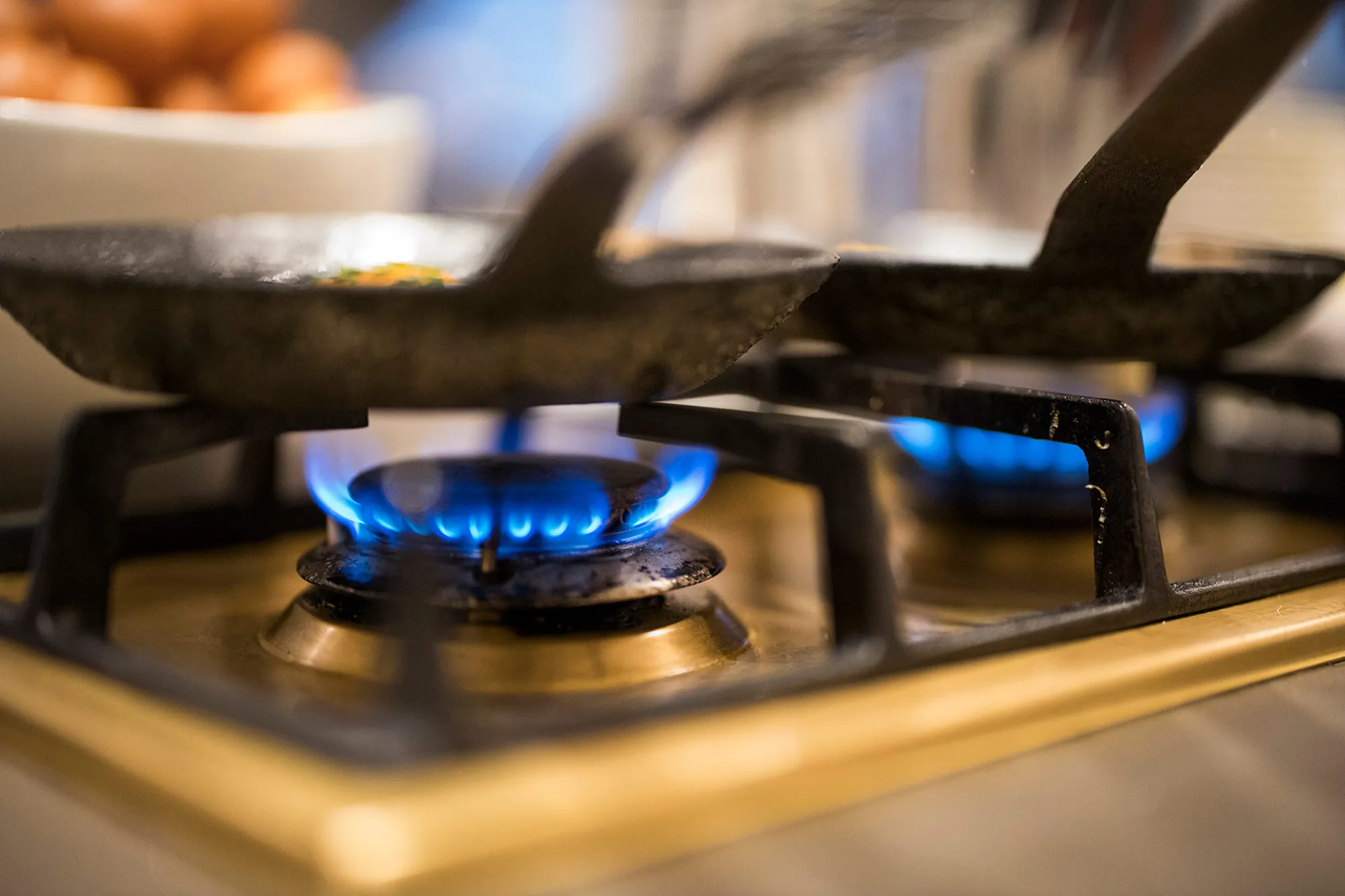 Gasherd mit zwei brennenden blauen Flammen unter Pfannen mit Kochlöffeln.