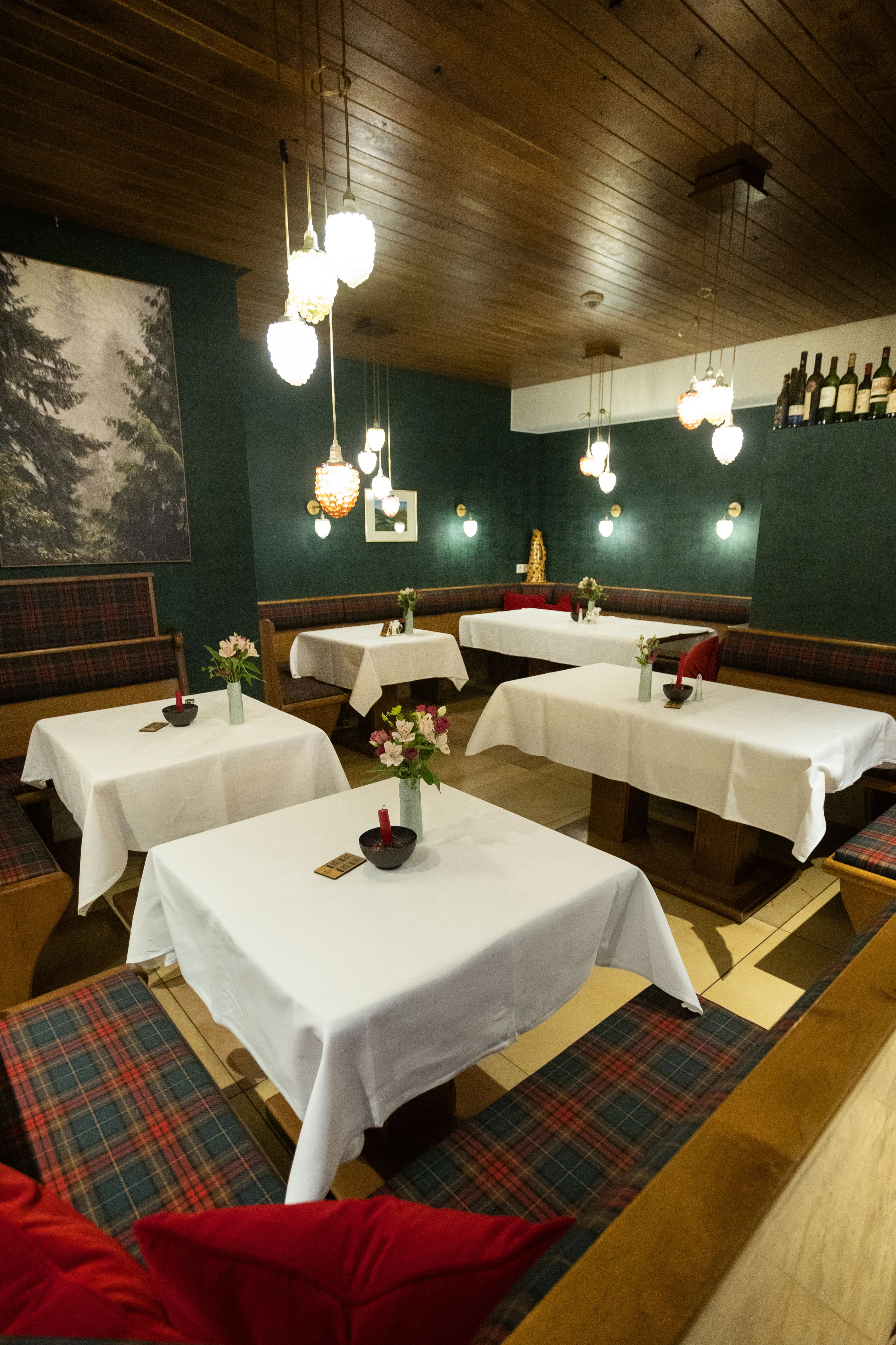 Gemütlicher Essbereich mit weißen Tischdecken, karierten Sitzbänken, roten Kissen und hängenden Lampen.