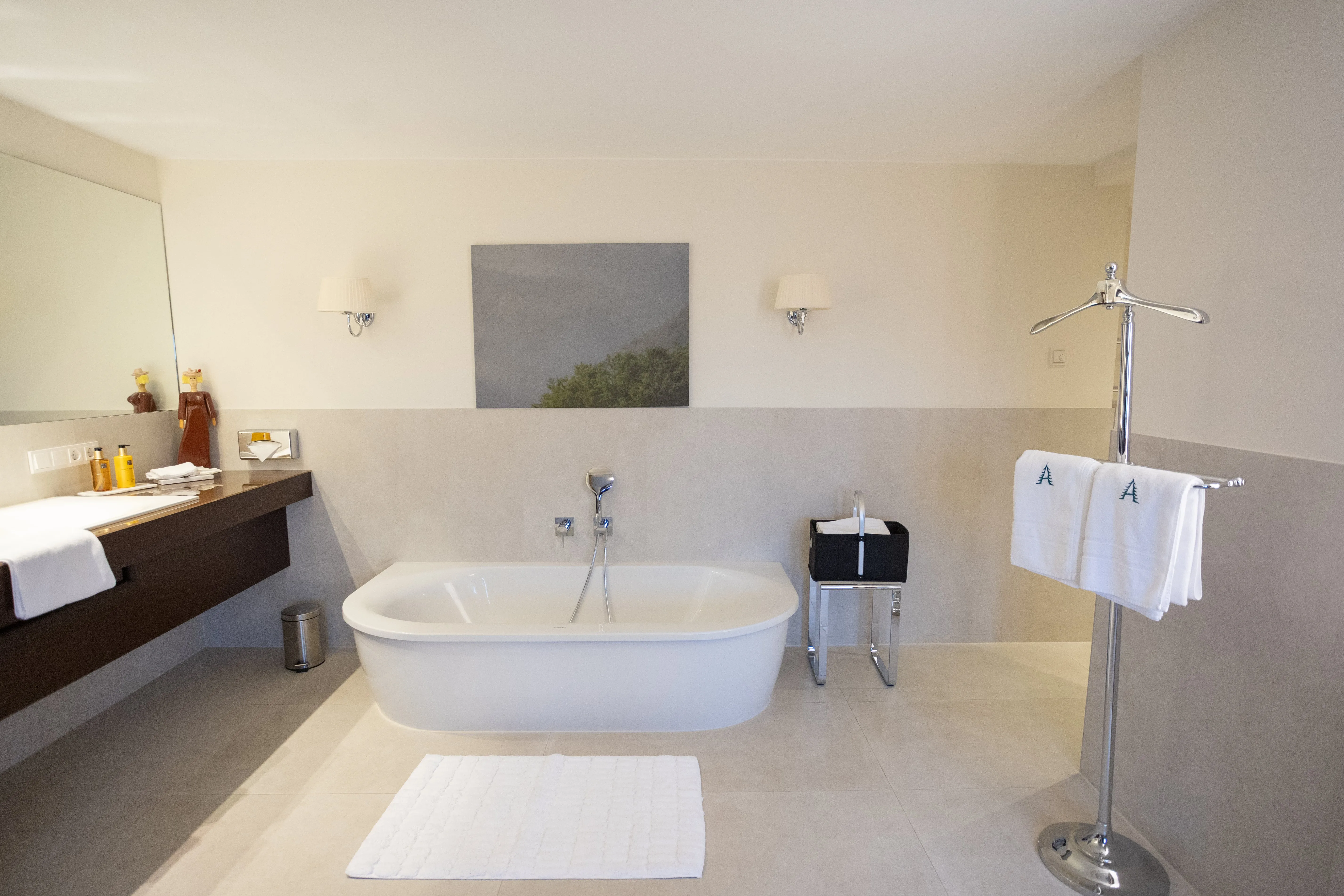 Modernes Badezimmer mit freistehender Badewanne, braunem Waschtisch, weißen Handtüchern und minimalistischem Design.