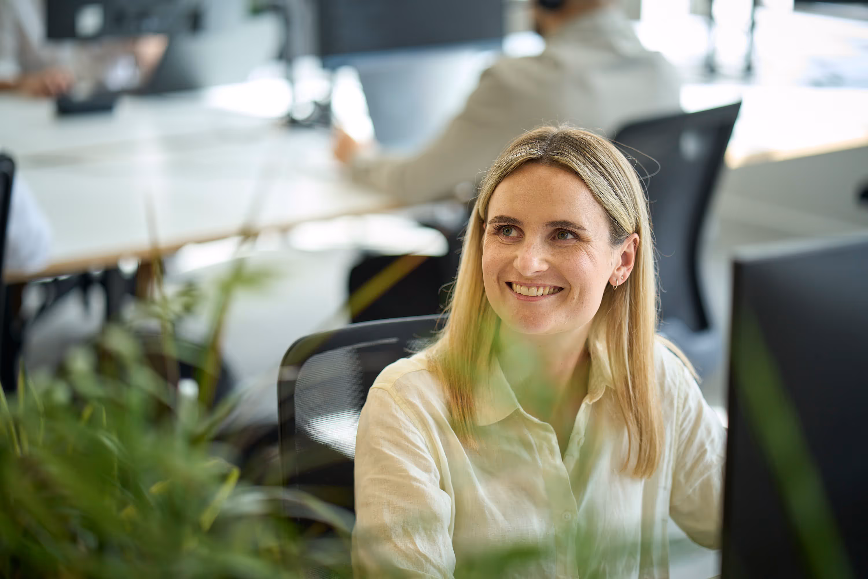 Smiling woman with blonde hair sitting at a desk in a modern office environment.