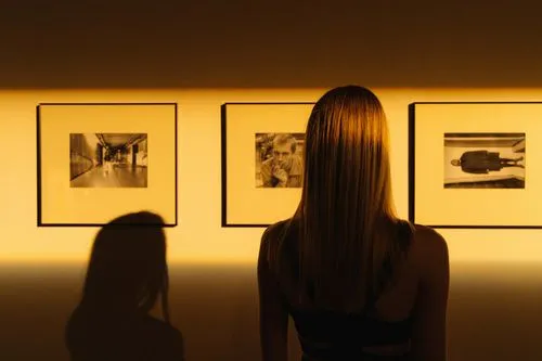 A woman observes framed black-and-white photographs in warm golden light