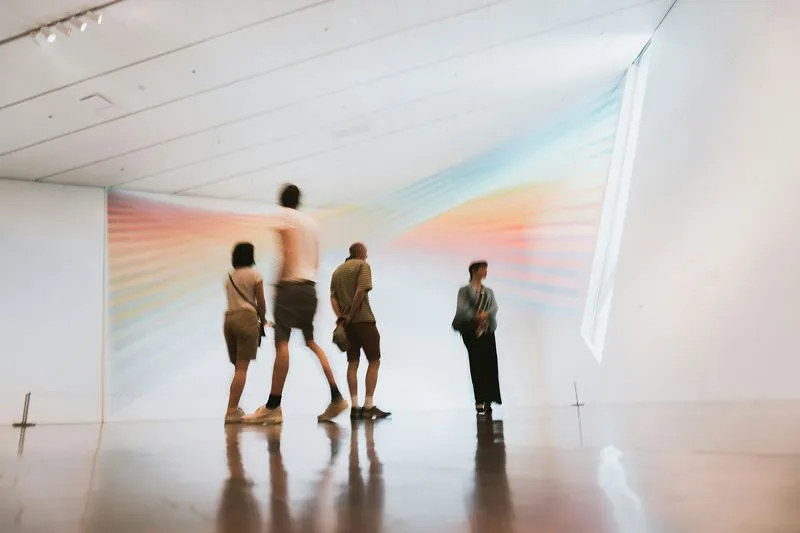 Blurry silhouettes of people in an art gallery with a colorful abstract wall installation