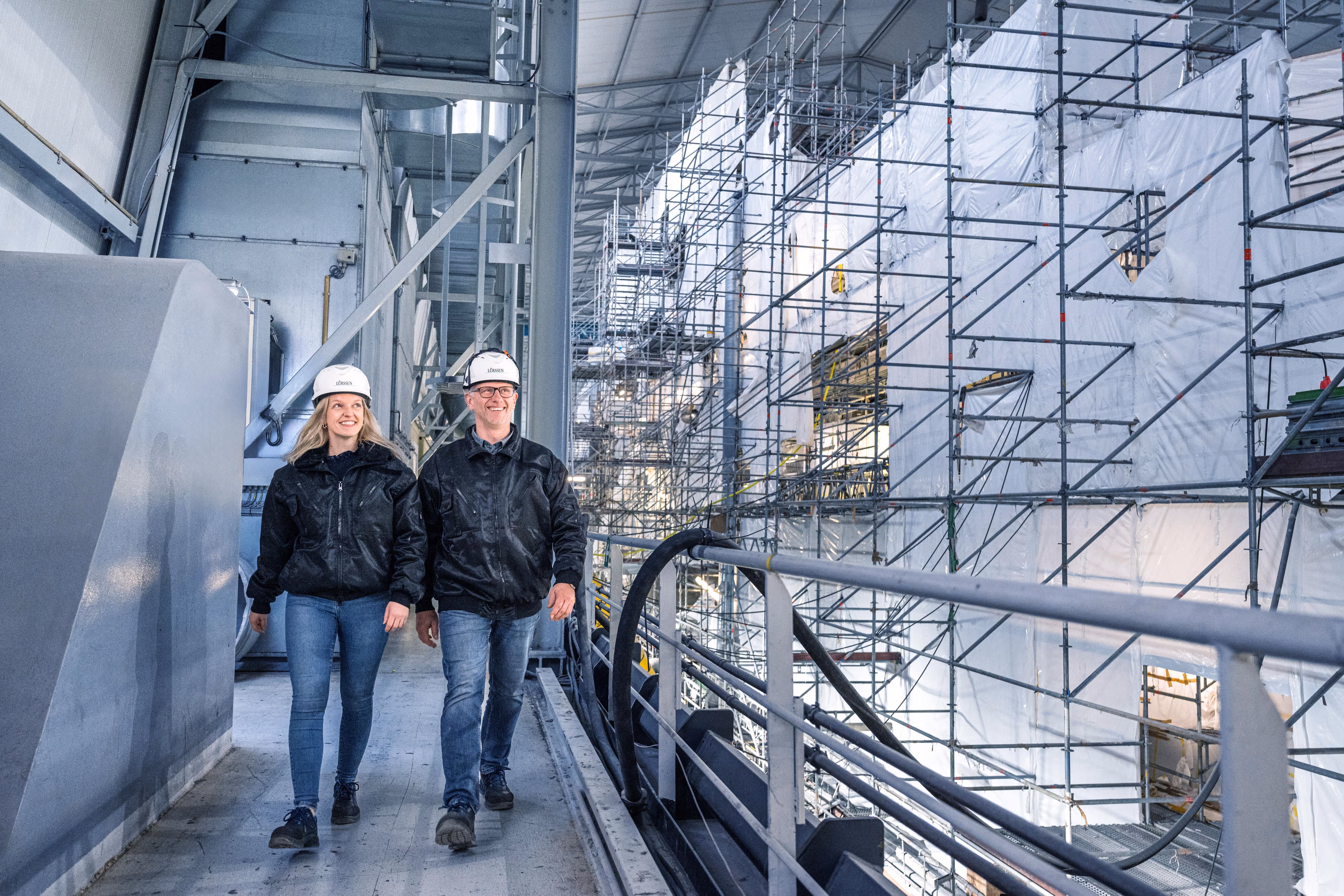 Ein Paar mit Helmen läuft in der Fabrikhalle umher