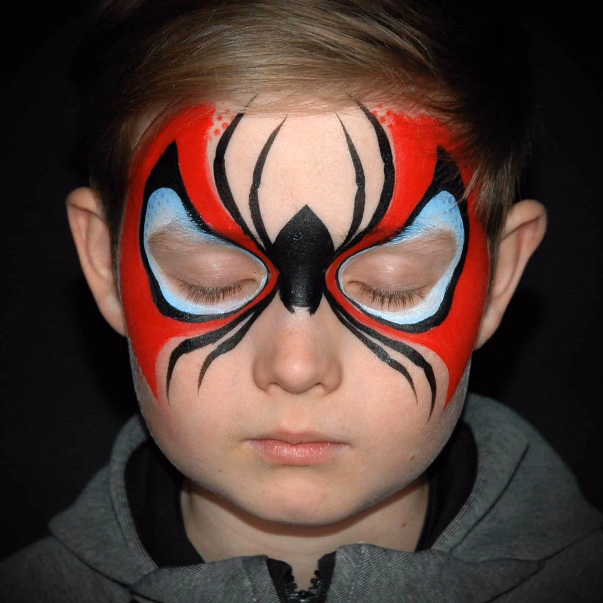 a boy with a starting of a spiderman face paint around his eyes and a painted spider in the middle