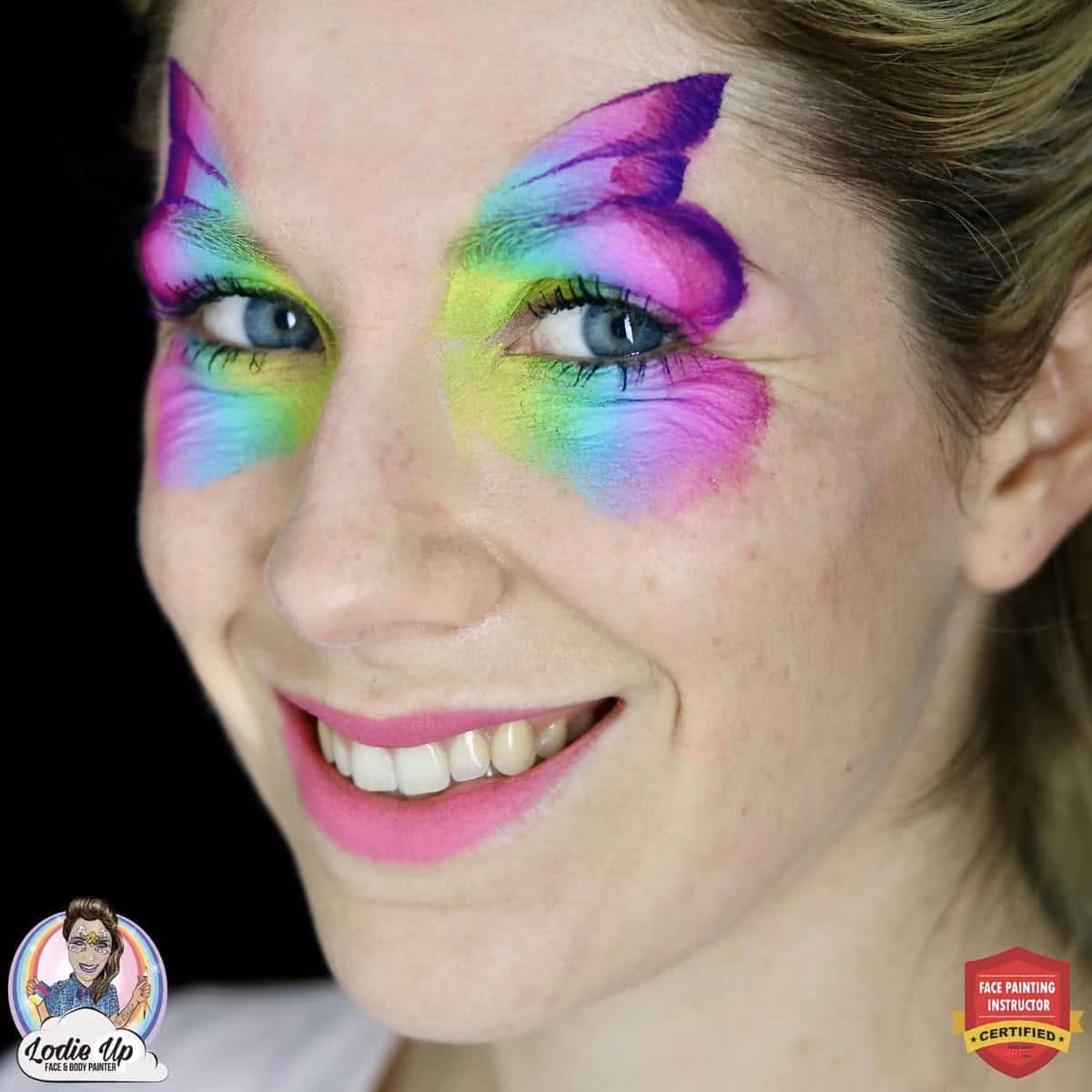 a side angle of a smiling woman thats in a process of having a coloful butterfly painted on her face