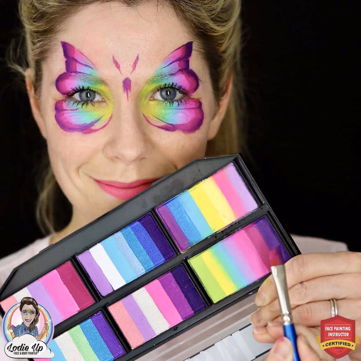 a woman with a colorful butterfly face paint holding a palette of shiny bright colors