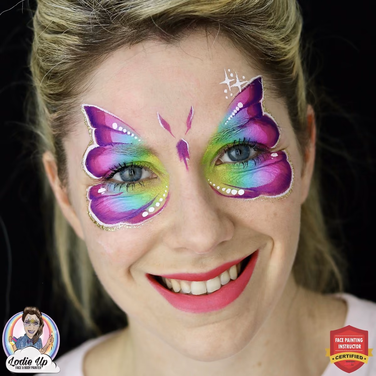 smiling woman looking at the camera with a gradient purple, blue and green butterfly face painting on her