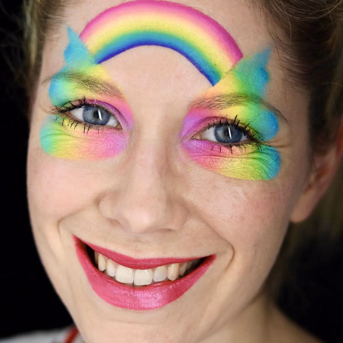 a woman with a base of a rainbow butterfly face paint on and around her eyes with a rainbow connecting them