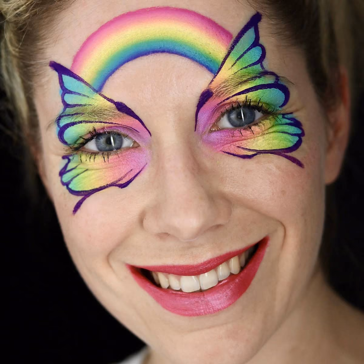 a woman with an hard outlined and almost compleated rainbow butterfly face paint design