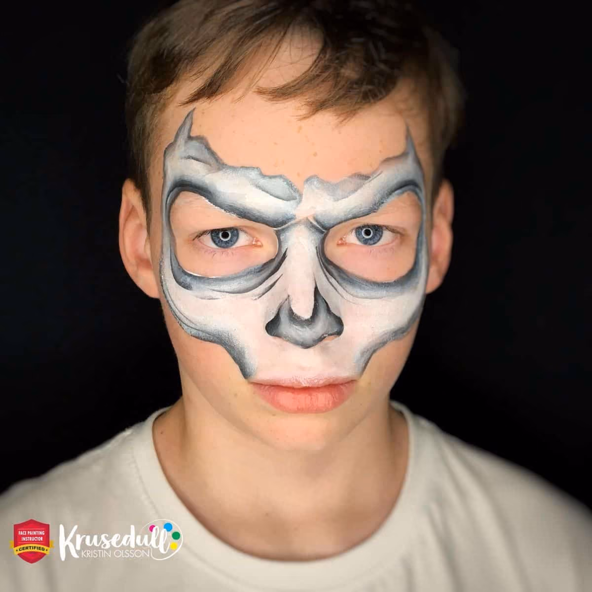a boy looking at the camera with an almost finished design of a skull face painting
