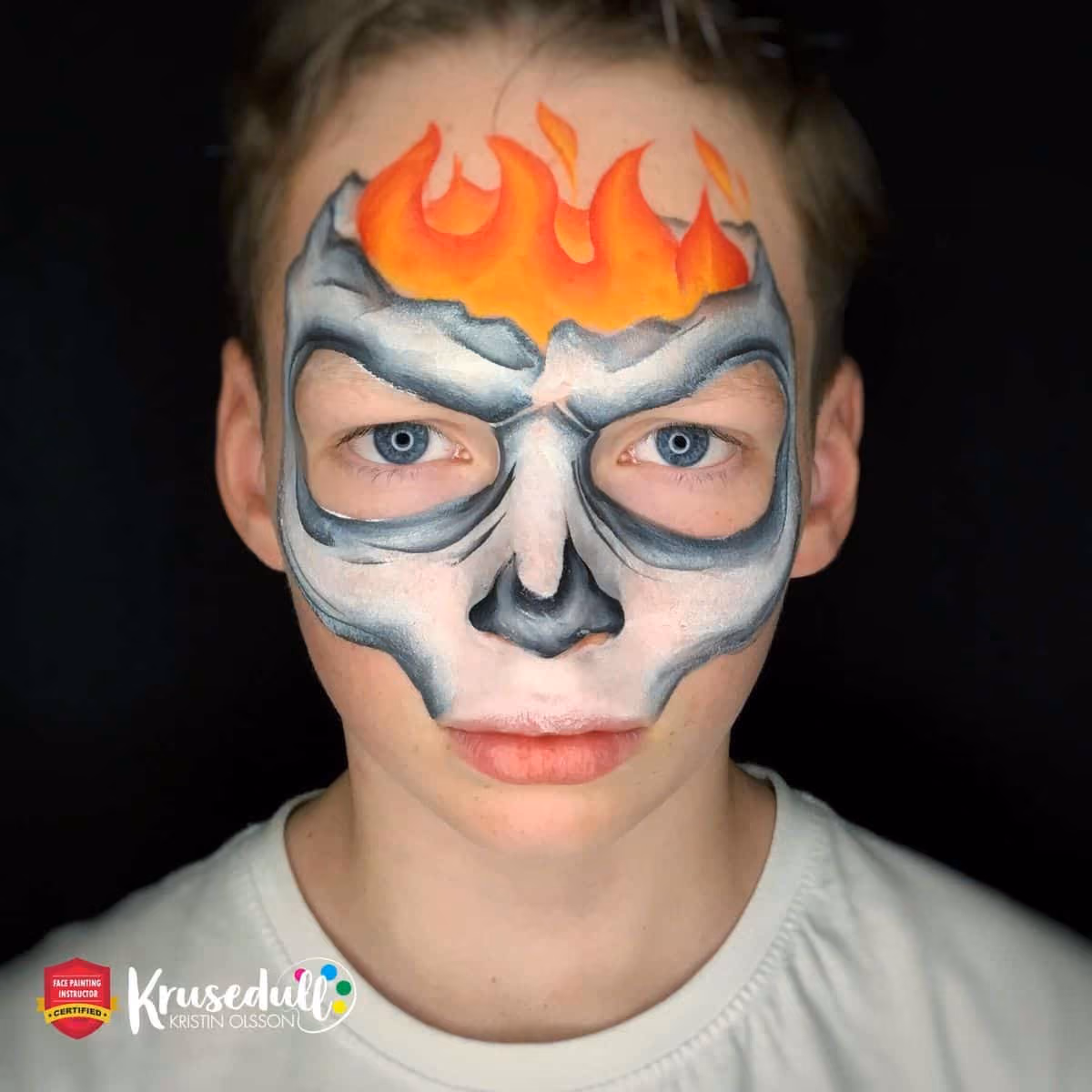 a boy with an uncomplete skull face paint around his face and flames on his forehead