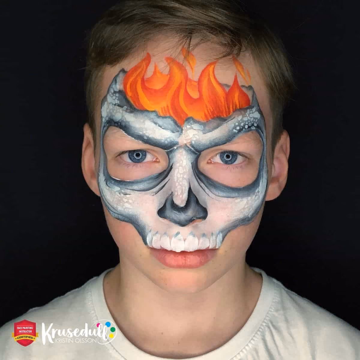 a boy looking at the camera with a flaming skull face paint design on his face
