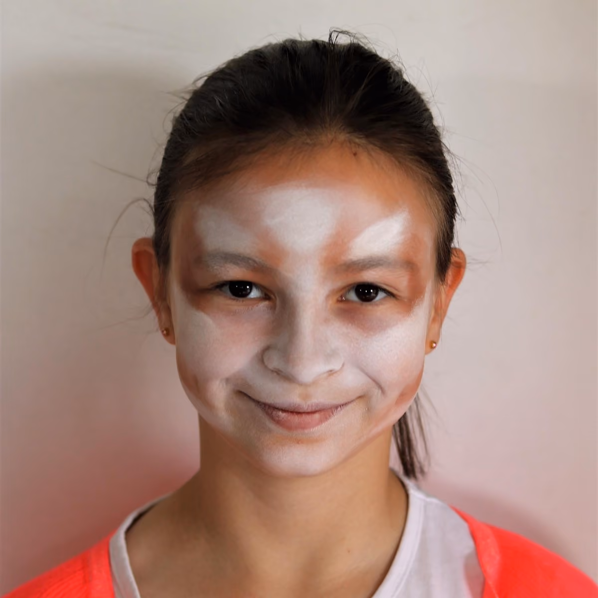 a girl looking directly at the camera with a skeleton face painting white colored base on her face