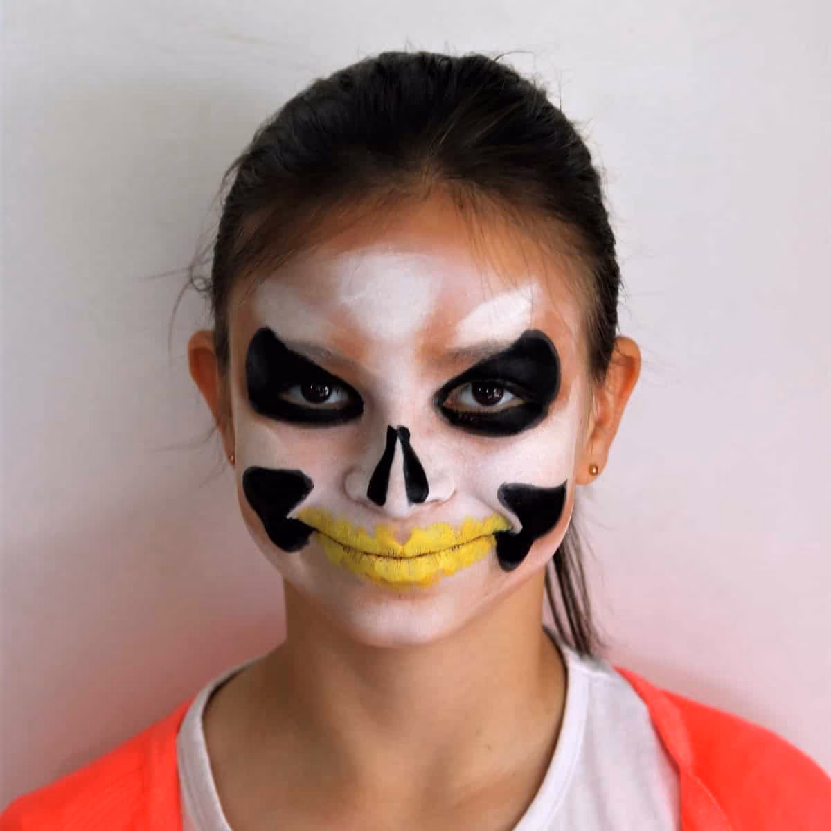 a girl with a skeleton face painting now with added black color around her eyes and cheeks and yellow color on her lips