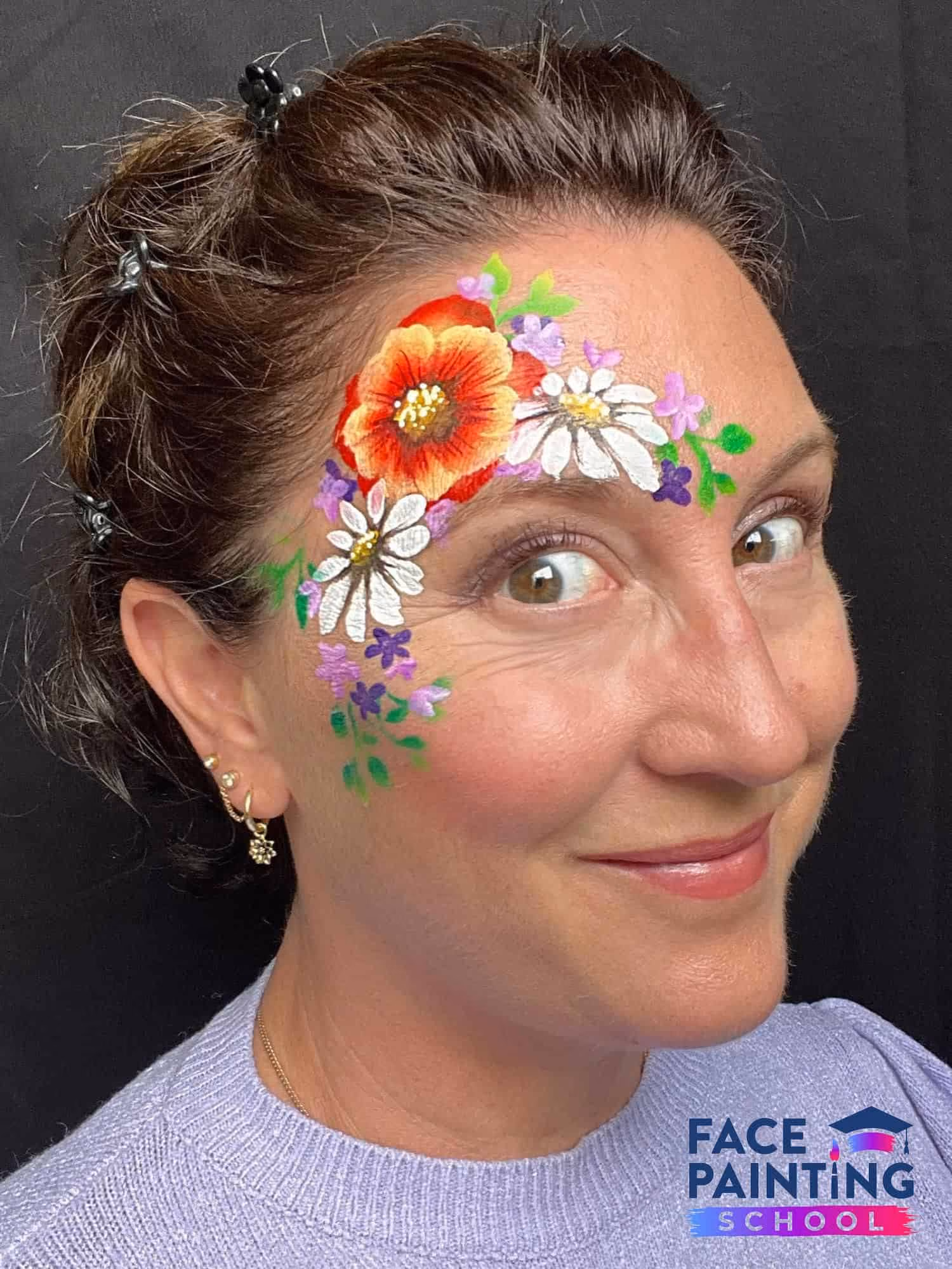 woman with her eyes wide open with three big flowers painted and more smaller flowers around them on her face