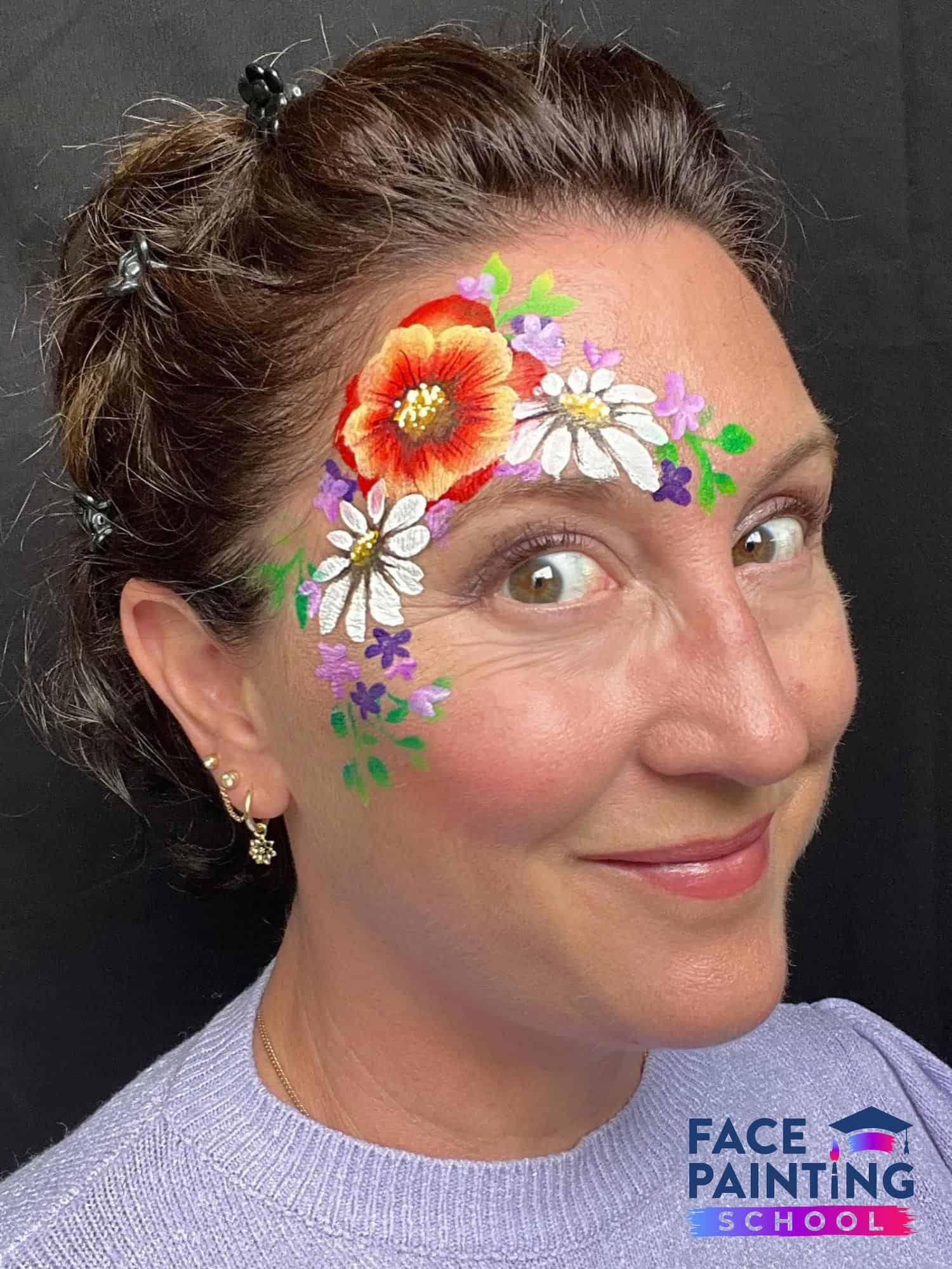 woman with her eyes wide open with three big flowers painted and more smaller flowers around them on her face