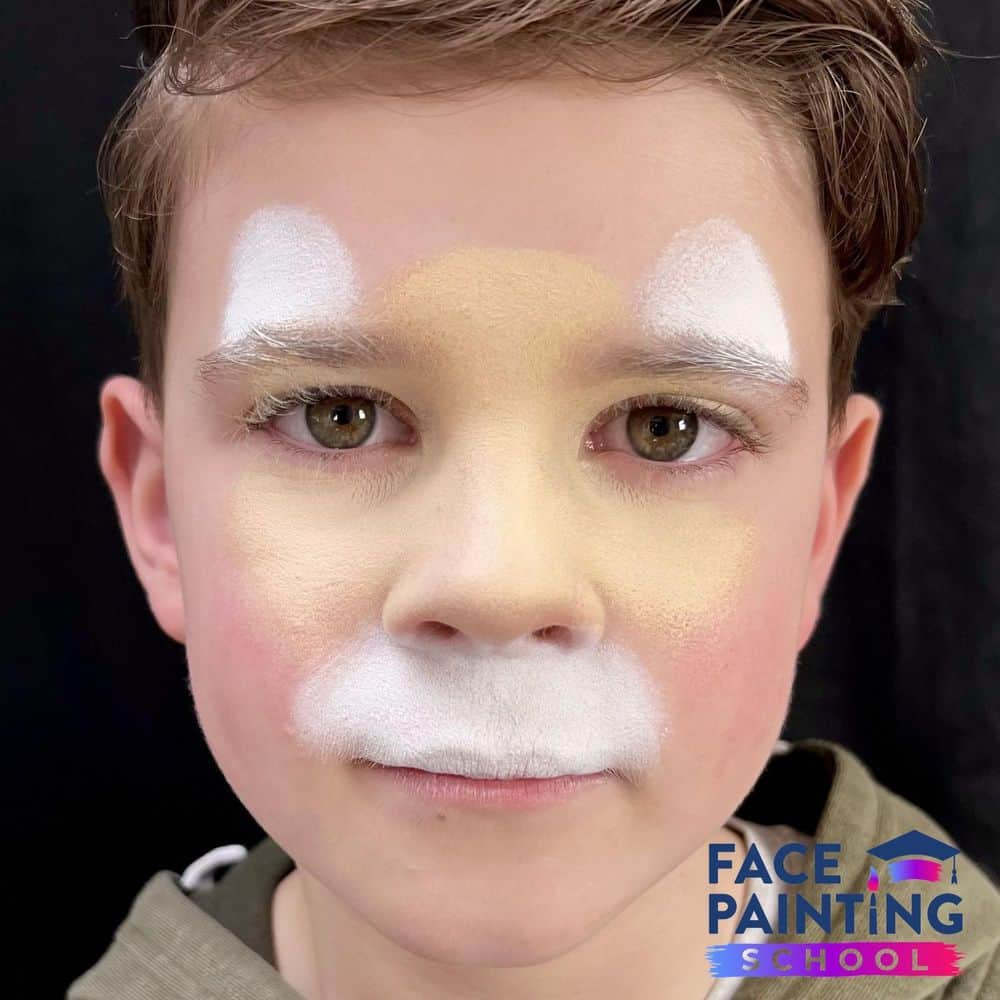 a boy with a starting base of a cheetah face paint on him