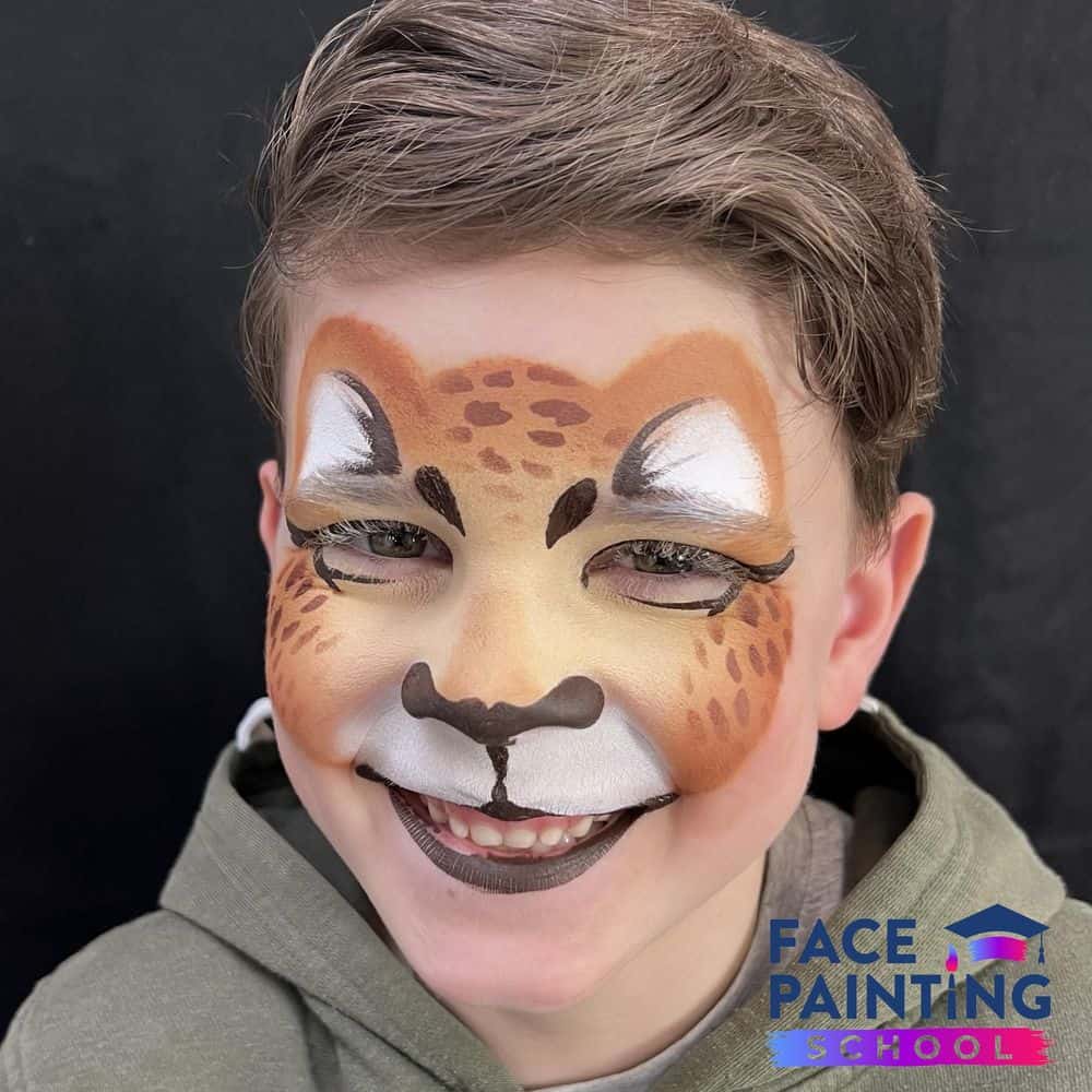 a smiling boy wearing a cheetach face paint design