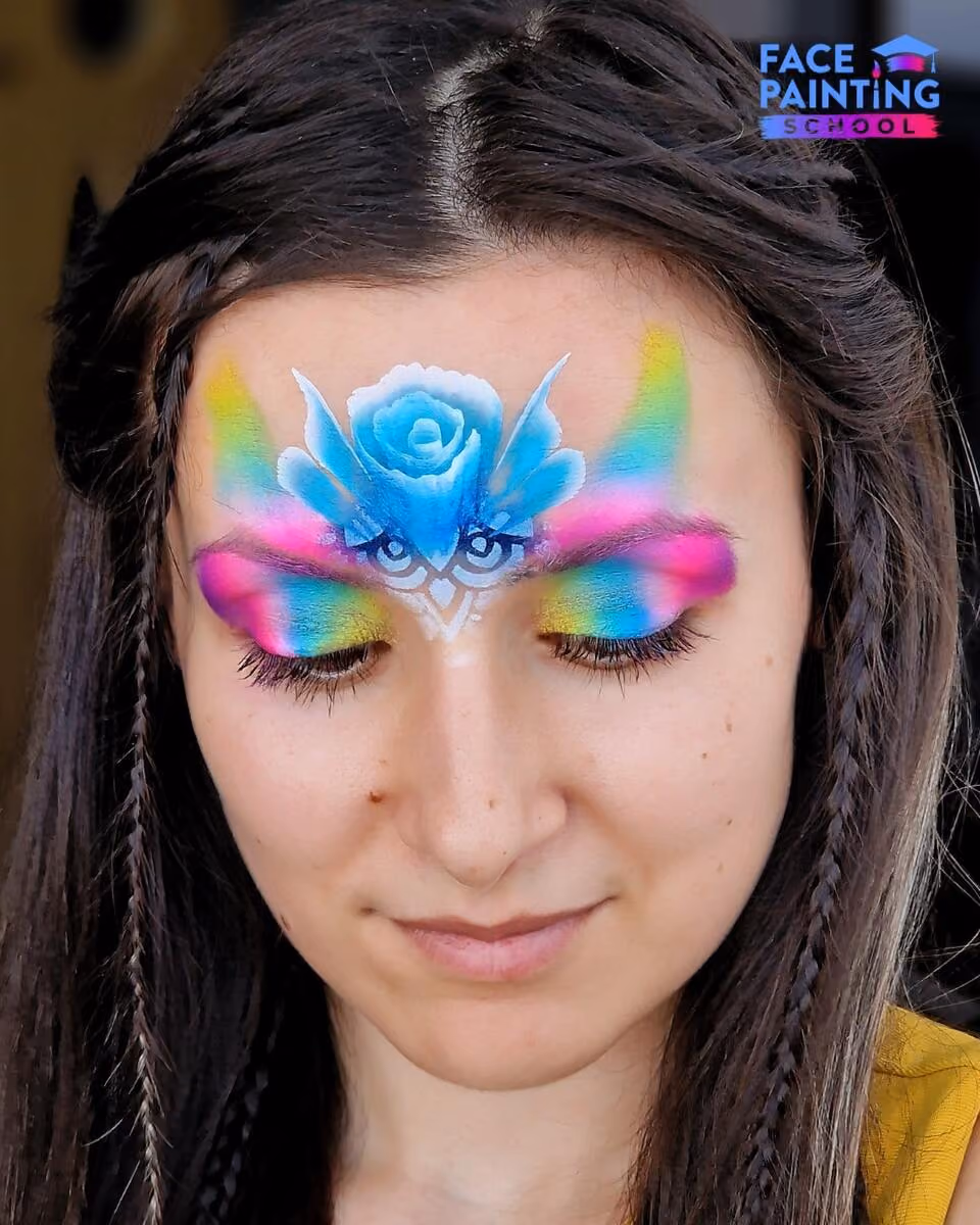 a woman with a shiny rainbow colored paint over her eyes with a blue flower on her forehead
