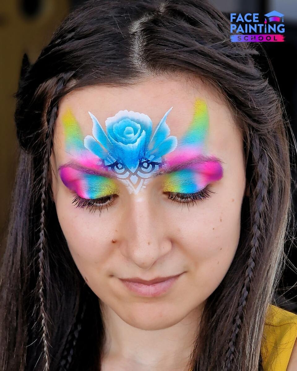 a woman with a shiny rainbow colored paint over her eyes with a blue flower on her forehead
