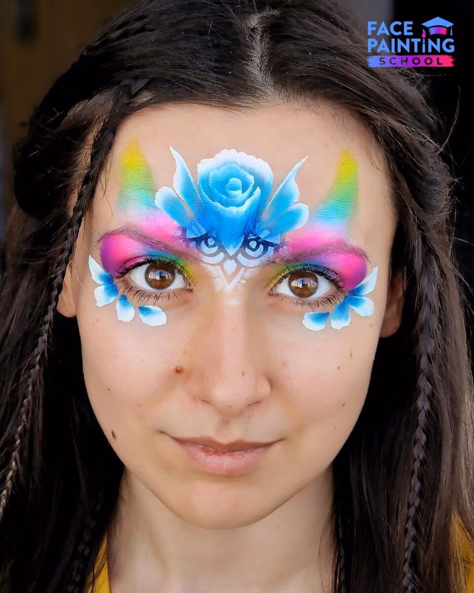 a woman with a shiny rainbow colored paint over her eyes with a blue flower on her forehead and leaves below her eyes