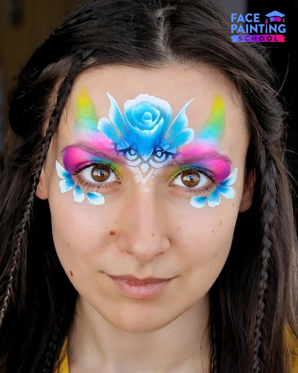 a woman with a shiny rainbow colored paint over her eyes with a blue flower on her forehead and leaves below her eyes