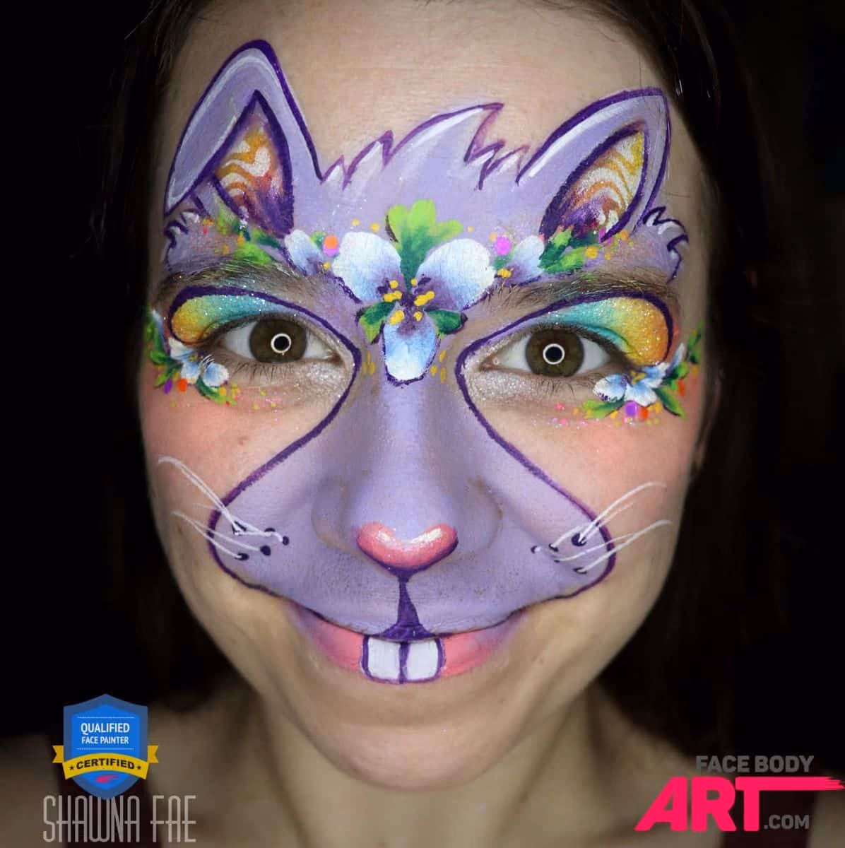 a smiling girl with a compleated bunny face paint desing over her face