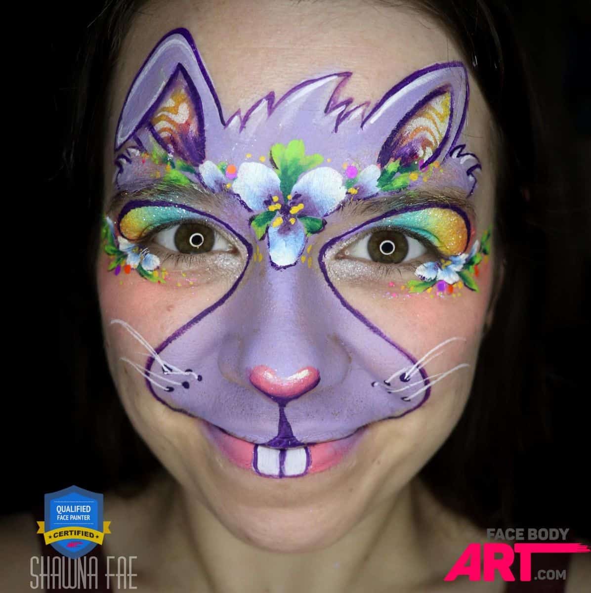 a smiling girl with a compleated bunny face paint desing over her face