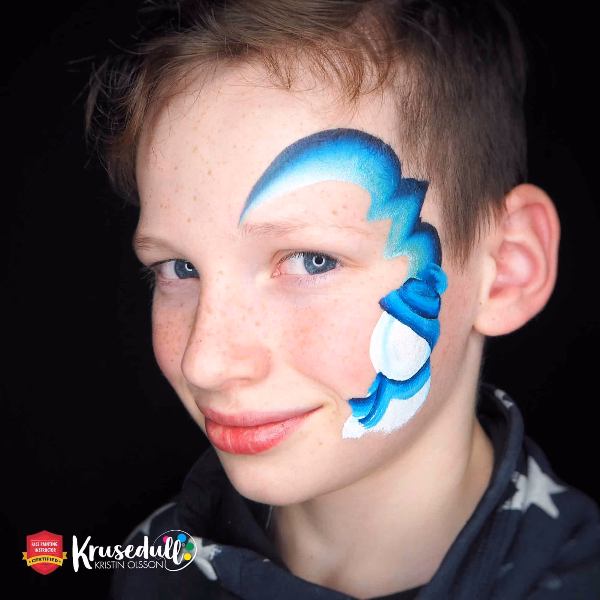 a boy with blue lines painted around his left eye and a base of the snowman with a scarf and a hat
