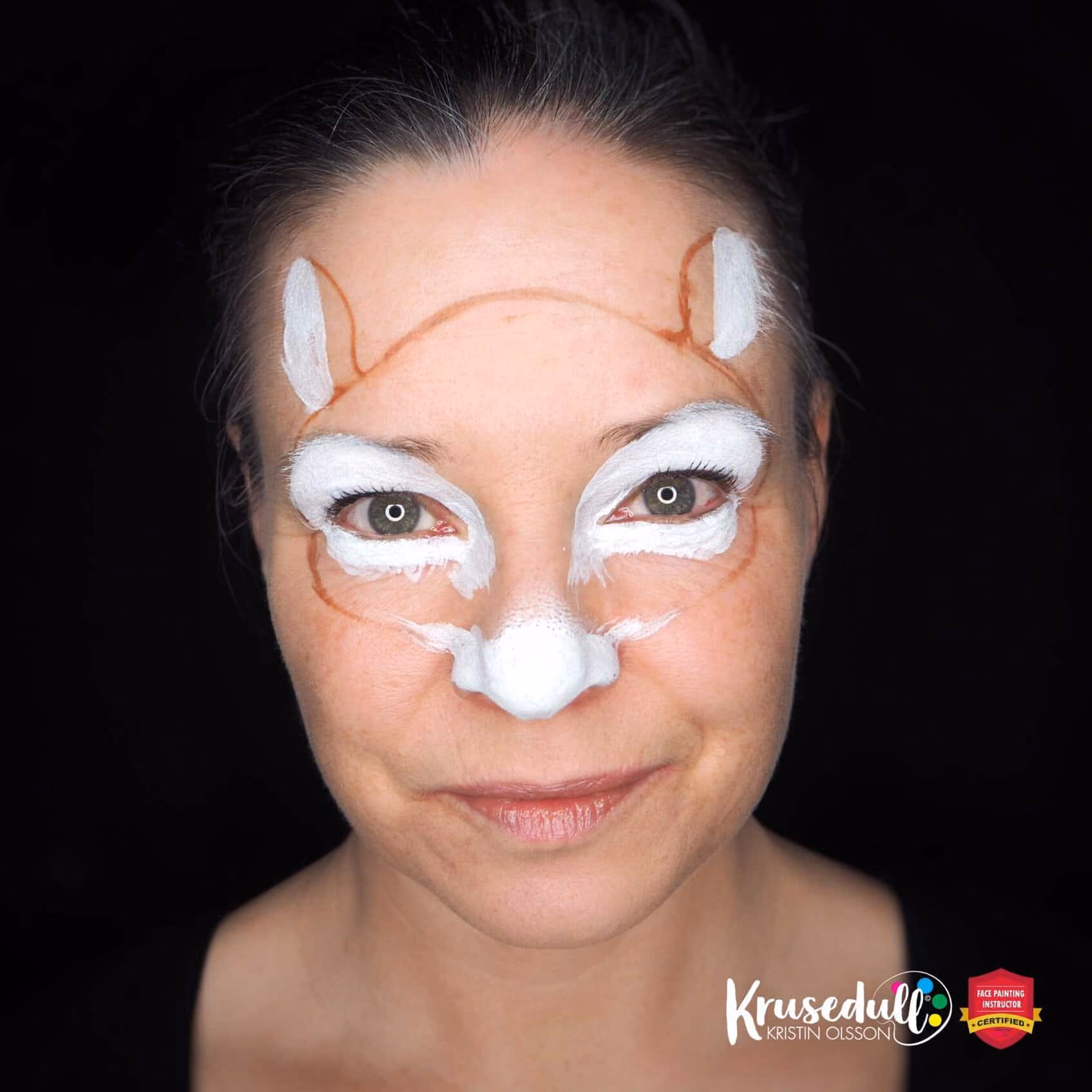 woman looking at the camera with a conture of a reindeer painted on her face and white paint on her nose, eyes and forehead