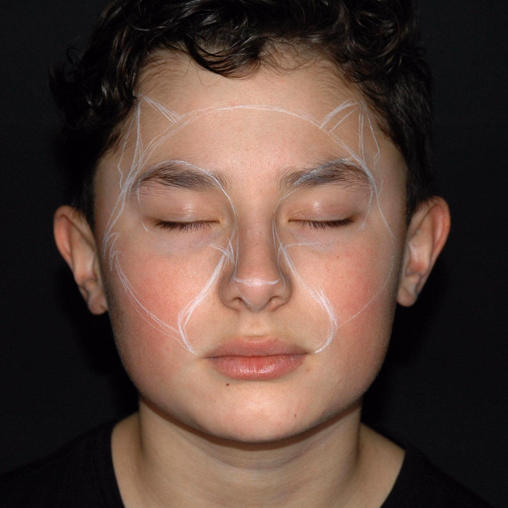 a boy with his eyes closed with a soft outline of the halloween cat face painting