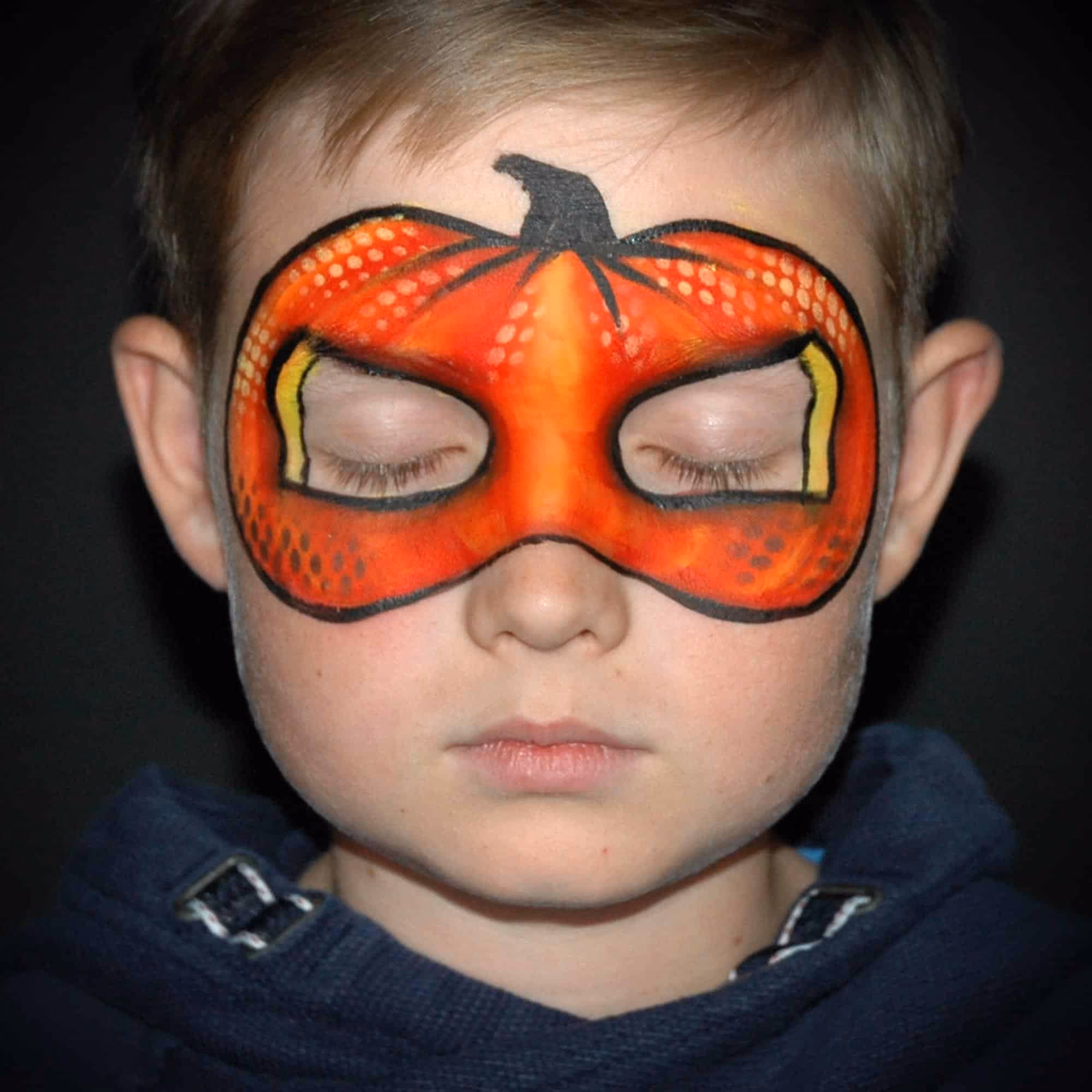 a boy with an almost finished orange pumpkin face paint around his eyes